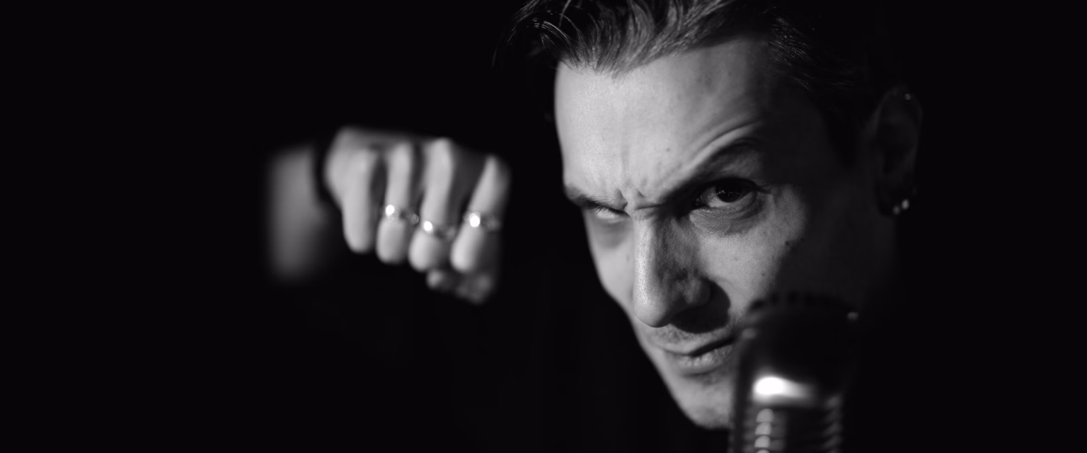 Portrait noir et blanc d'Adrien Larmande, comédien voix off Sonacom, poing tendu vers l'objectif, au micro vintage