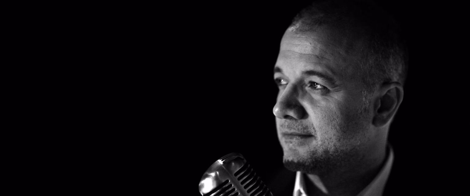 Portrait noir et blanc d'Alain Ghazal, comédien voix off Sonacom, de profil, le regard de côté, au micro vintage