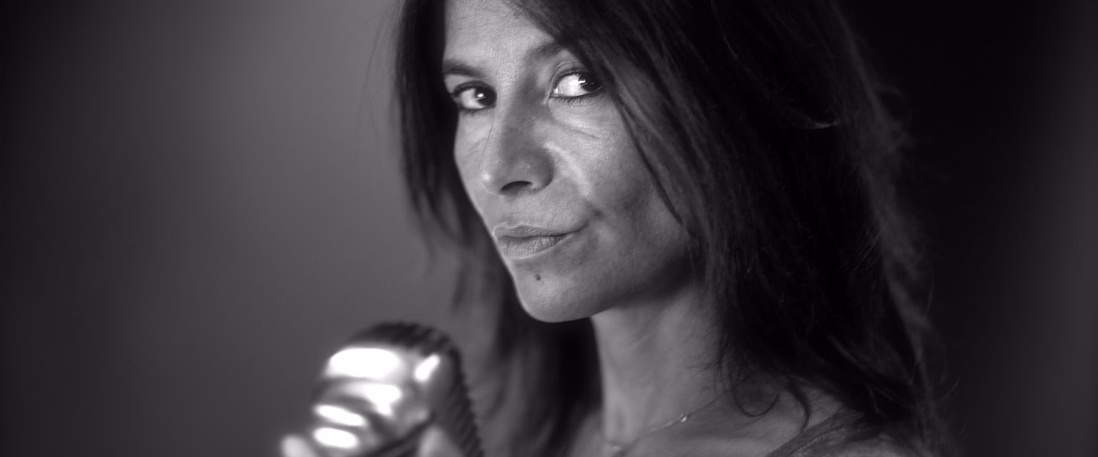 Portrait noir et blanc d'Anne Ferrier, comédienne voix off Sonacom, cheveux longs, le regard levé, au micro vintage