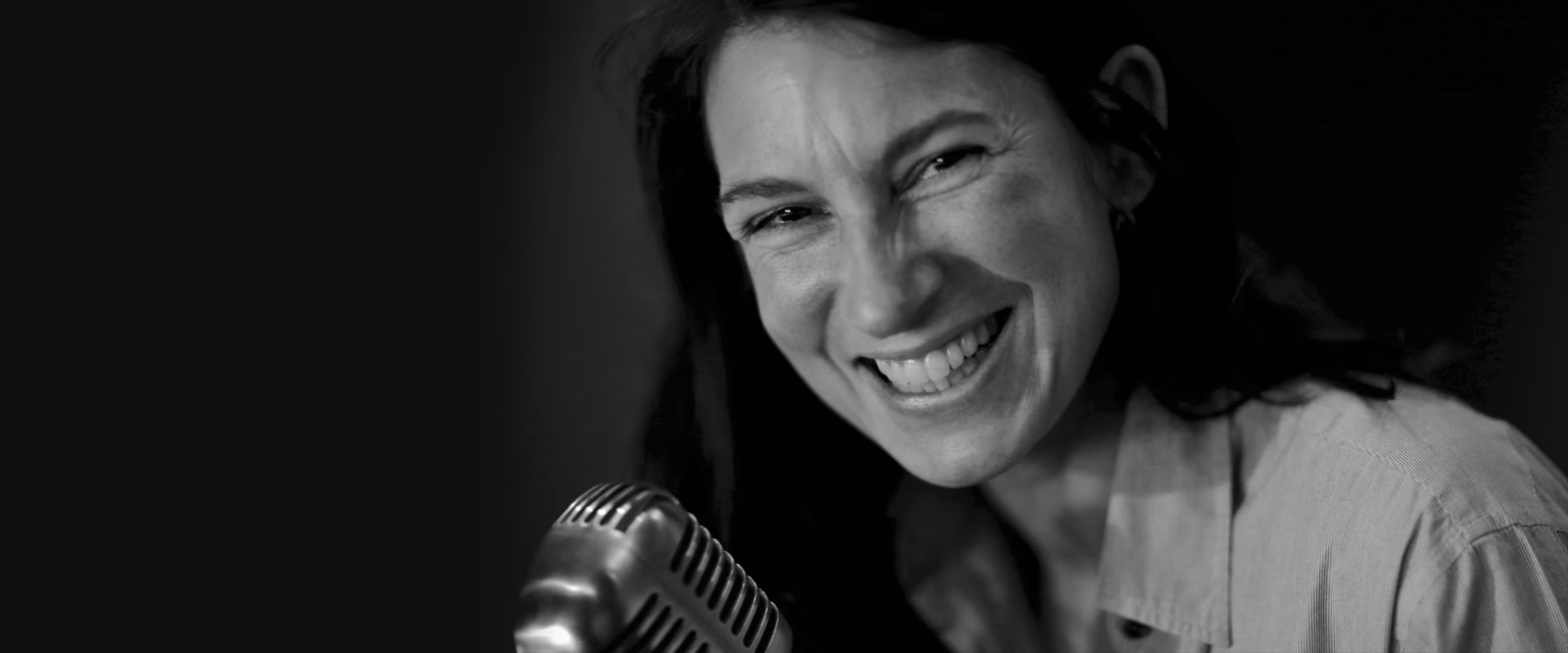 Portrait noir et blanc de Catherine Nullans, comédienne voix off Sonacom, en train de rire, au micro vintage