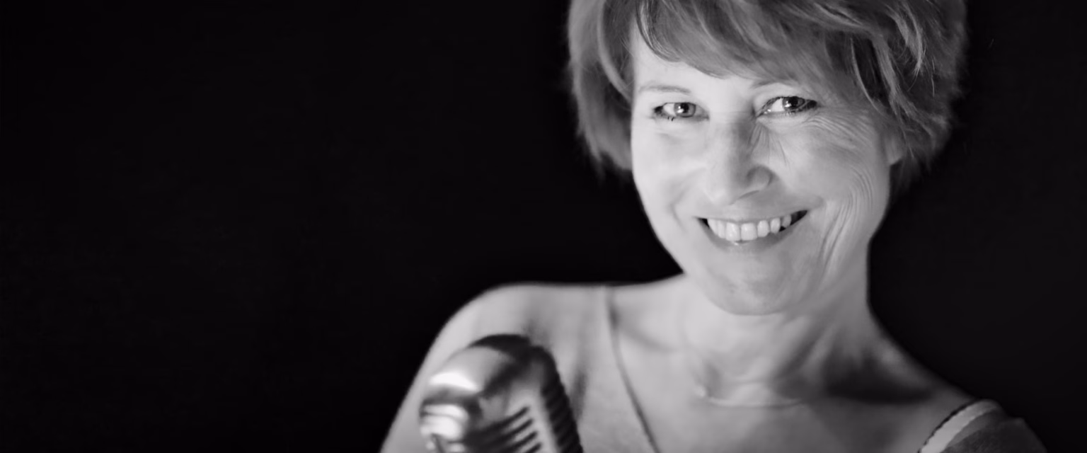 Portrait noir et blanc de Céline Monsarrat, comédienne voix off Sonacom, souriante, au micro vintage