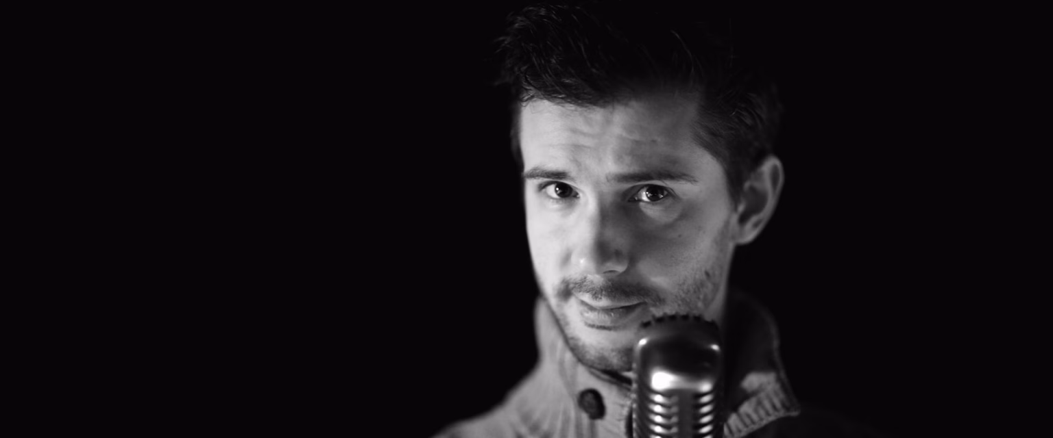Portrait noir et blanc de Donald Reignoux, comédien voix off Sonacom, le regard droit vers l'objectif, au micro vintage