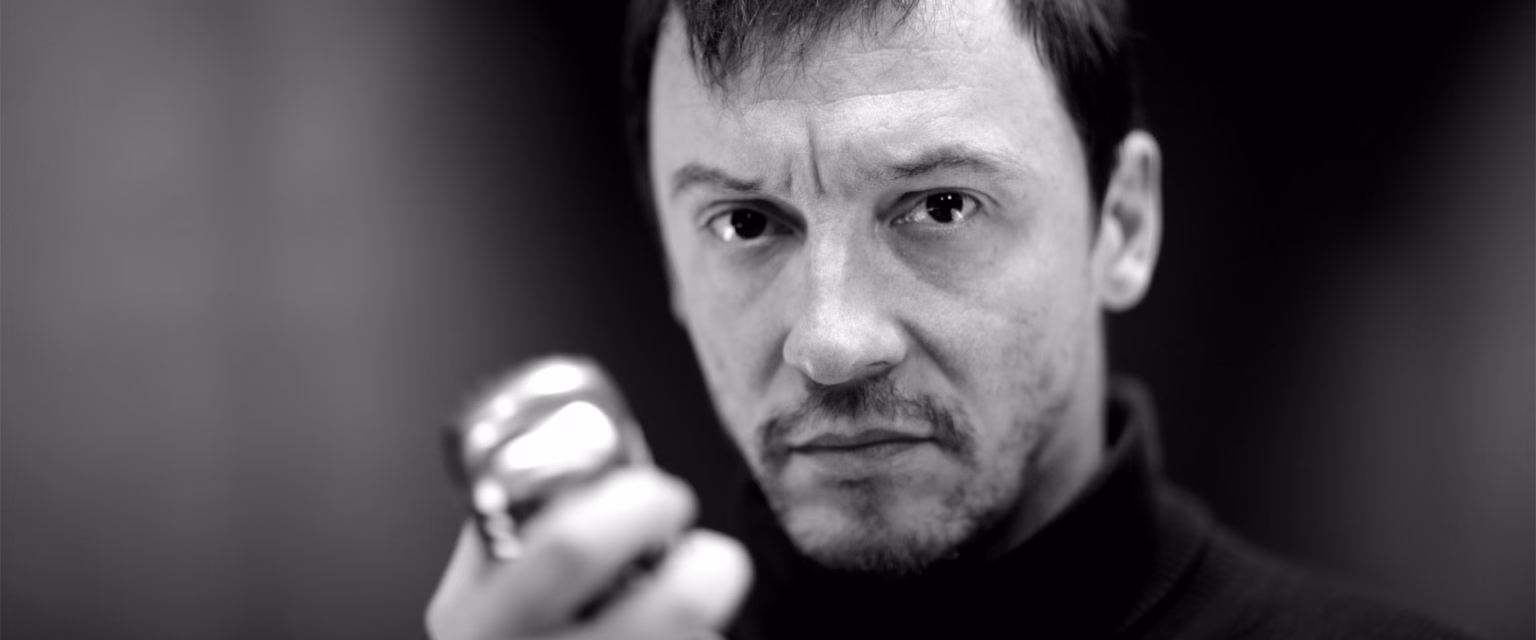 Portrait noir et blanc d'Emmanuel Curtil, comédien voix off Sonacom, en col roulé, le regard intense, au micro vintage