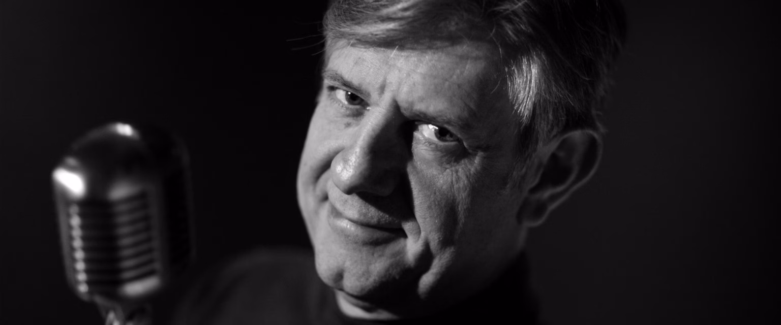 Portrait noir et blanc de François Berland, comédien voix off Sonacom, le sourire en coin, au micro vintage