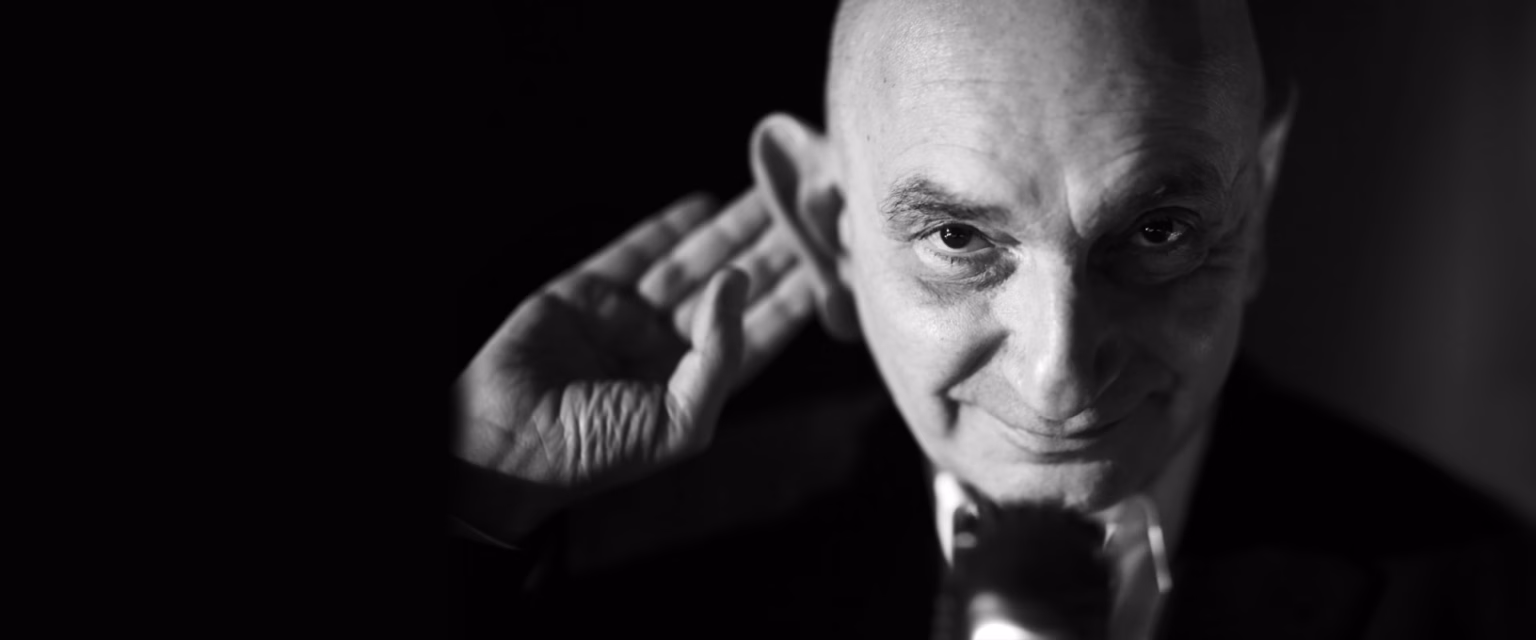 Portrait noir et blanc de Jacky Nercessian, comédien voix off Sonacom, la main près de l'oreille, au micro vintage