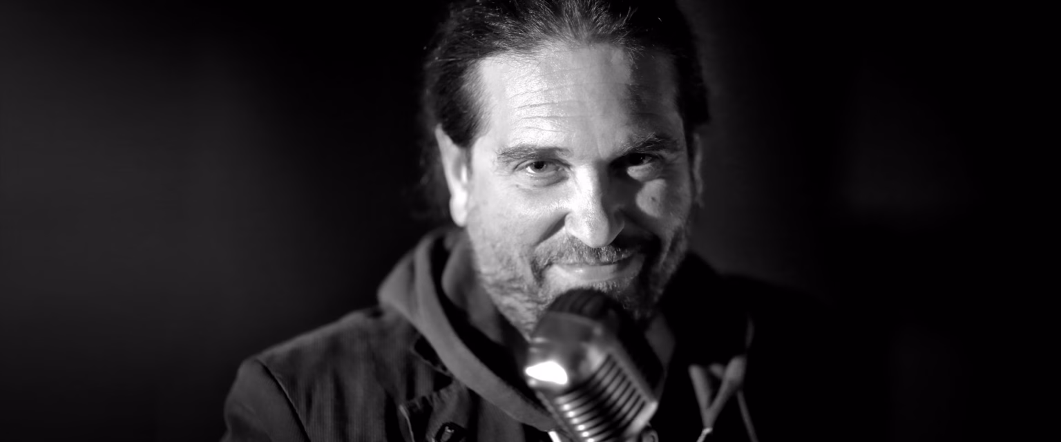 Portrait noir et blanc de Mark Lesser, comédien voix off Sonacom, barbe et parka, au micro vintage