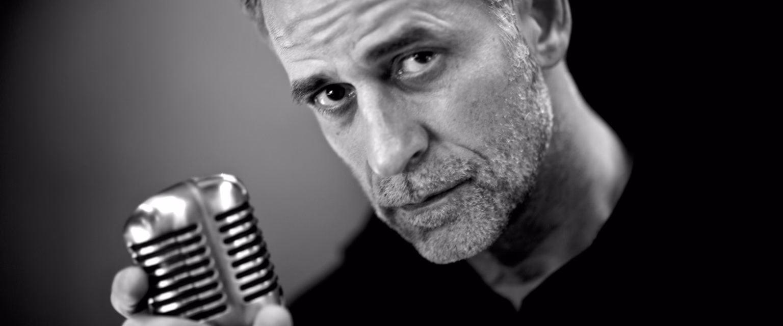 Portrait noir et blanc d'Olivier Perrot, comédien voix off Sonacom, le micro vintage à la main, le regard droit