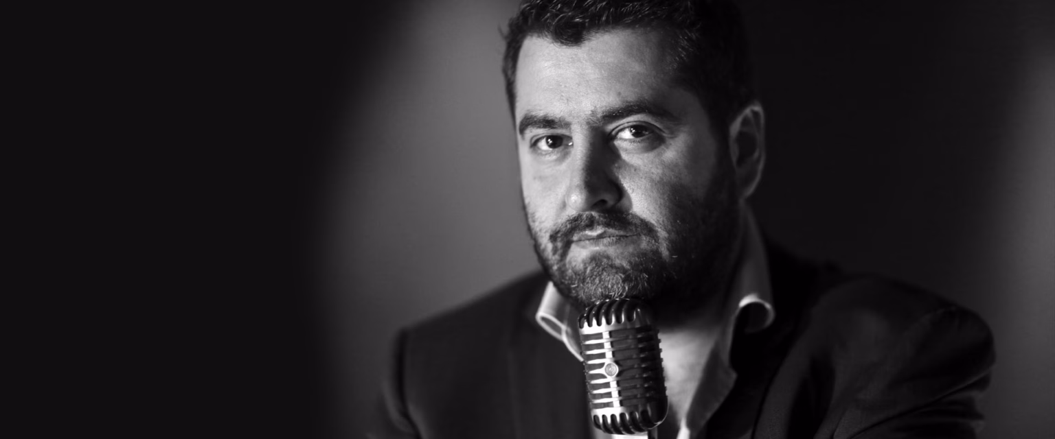 Portrait noir et blanc de Philippe Llado, comédien voix off Sonacom, barbu, en veste sombre, au micro vintage