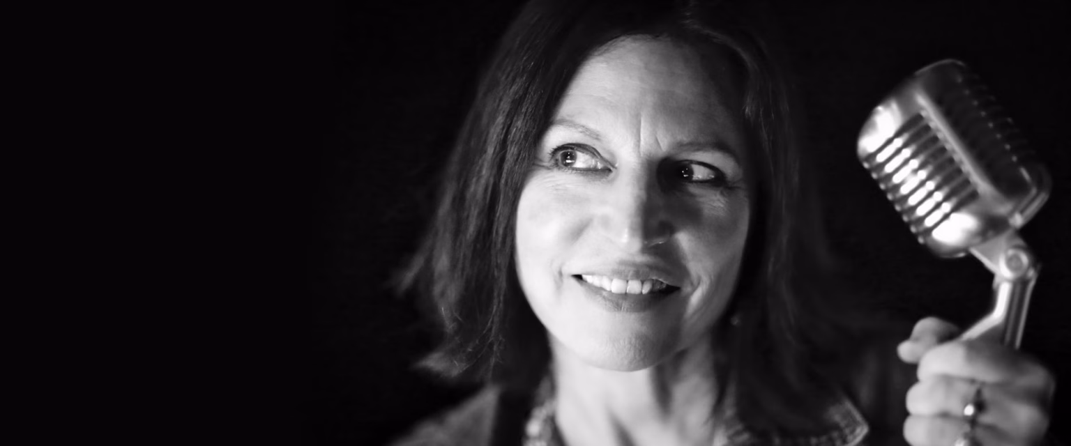 Portrait noir et blanc de Roxanne Frias, comédienne voix off Sonacom, souriante, le micro vintage à la main