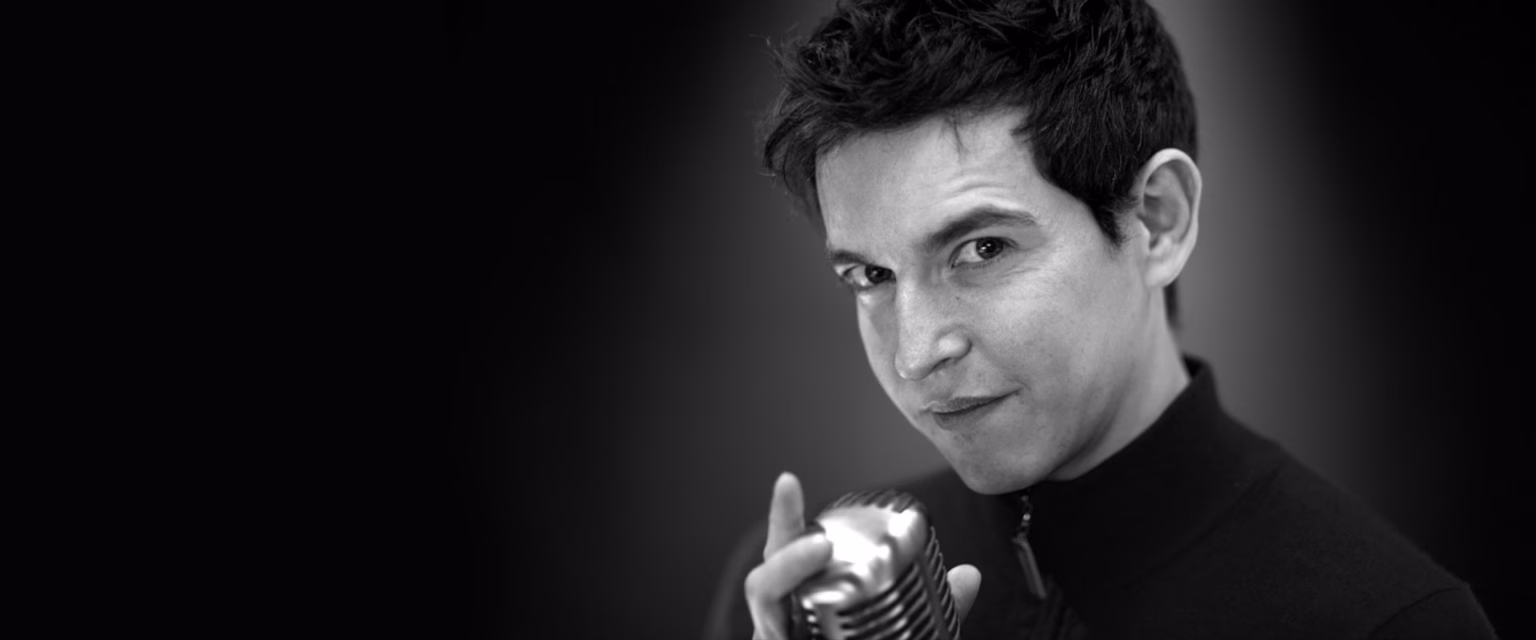 Portrait noir et blanc de Yoann Sover, comédien voix off Sonacom, le doigt levé, au micro vintage